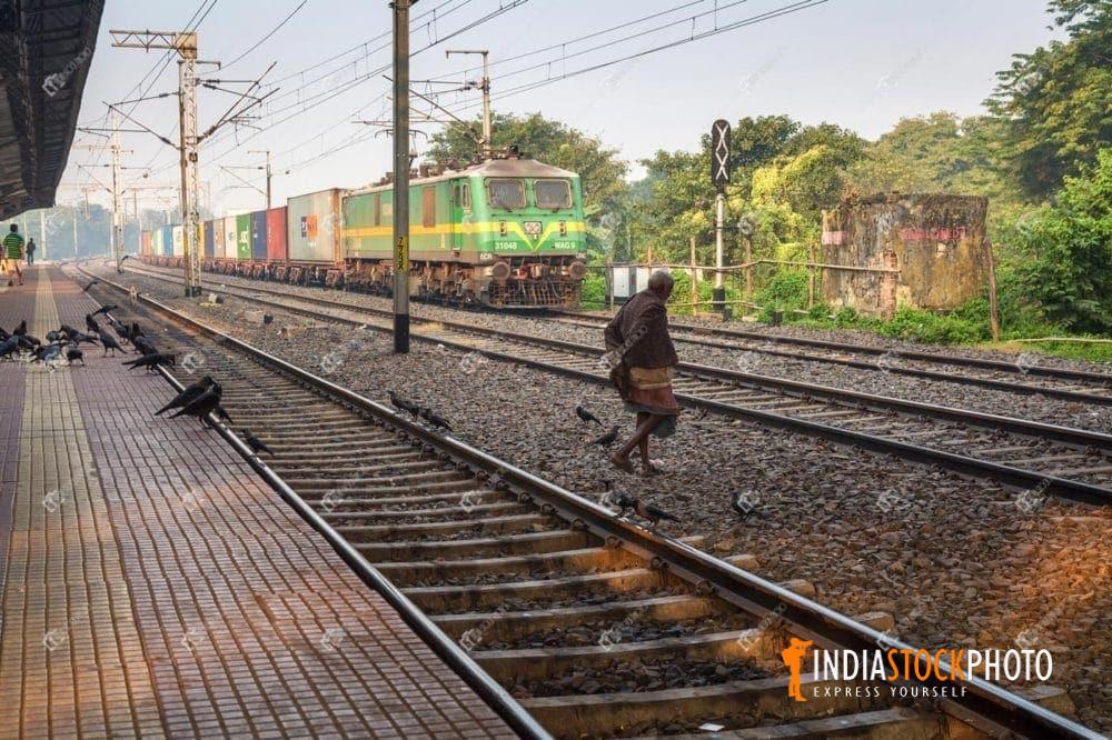 Old man crossing a railway track with a goods train at a railway platform