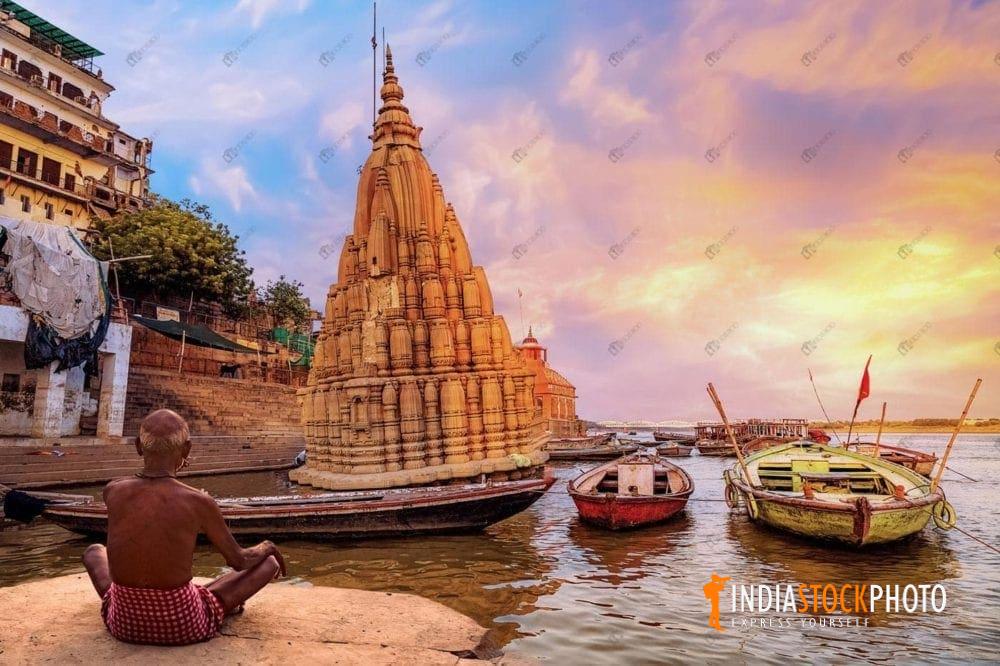 Old man meditates at the Varanasi Ganges riverbank at sunrise