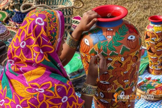 Rural Indian woman painting on a clay pitcher at handicraft fare