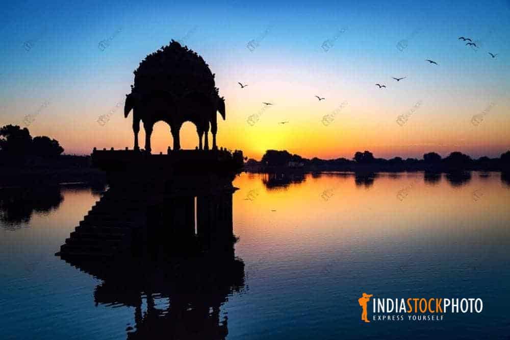Gadi Sagar lake Jaisalmer with ancient architecture in silhouette at sunrise