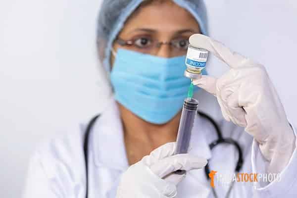 Indian doctor drawing medication into a syringe from a vaccine bottle