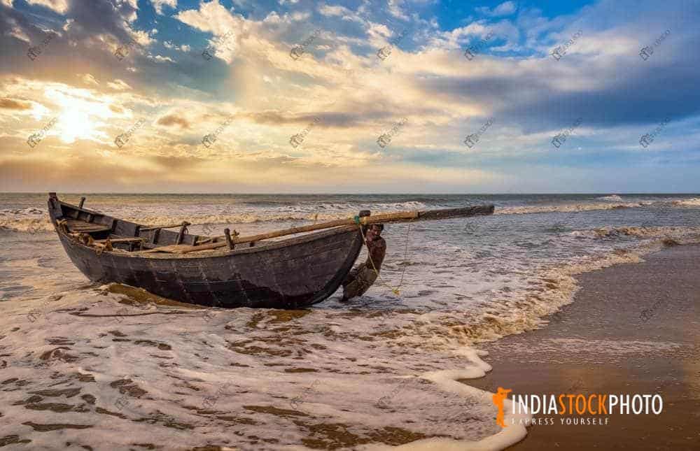 Indian fisherman tows his boat to sea shore at sunset