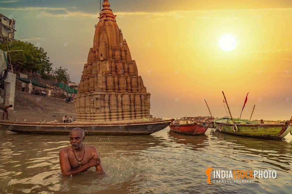 Man bathing in the Ganges river at Varanasi at sunrise with ancient architecture