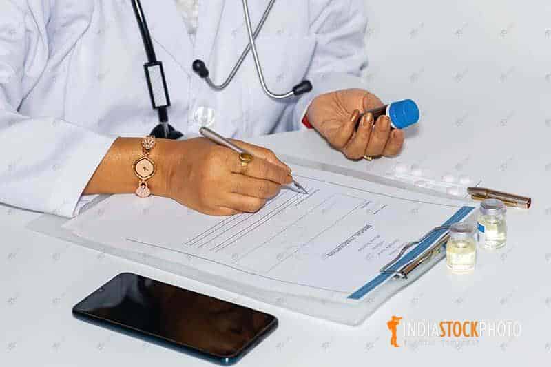 Doctor writing patient medical prescription holding a vaccine bottle